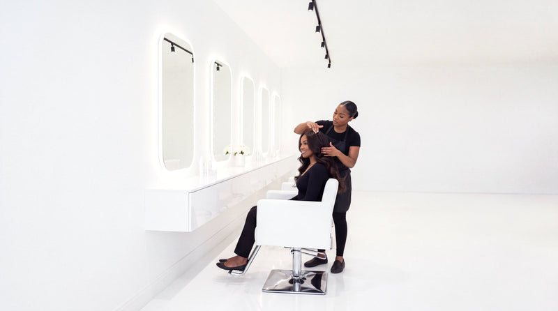 Stylist working on a client's raw hair extensions in a white salon